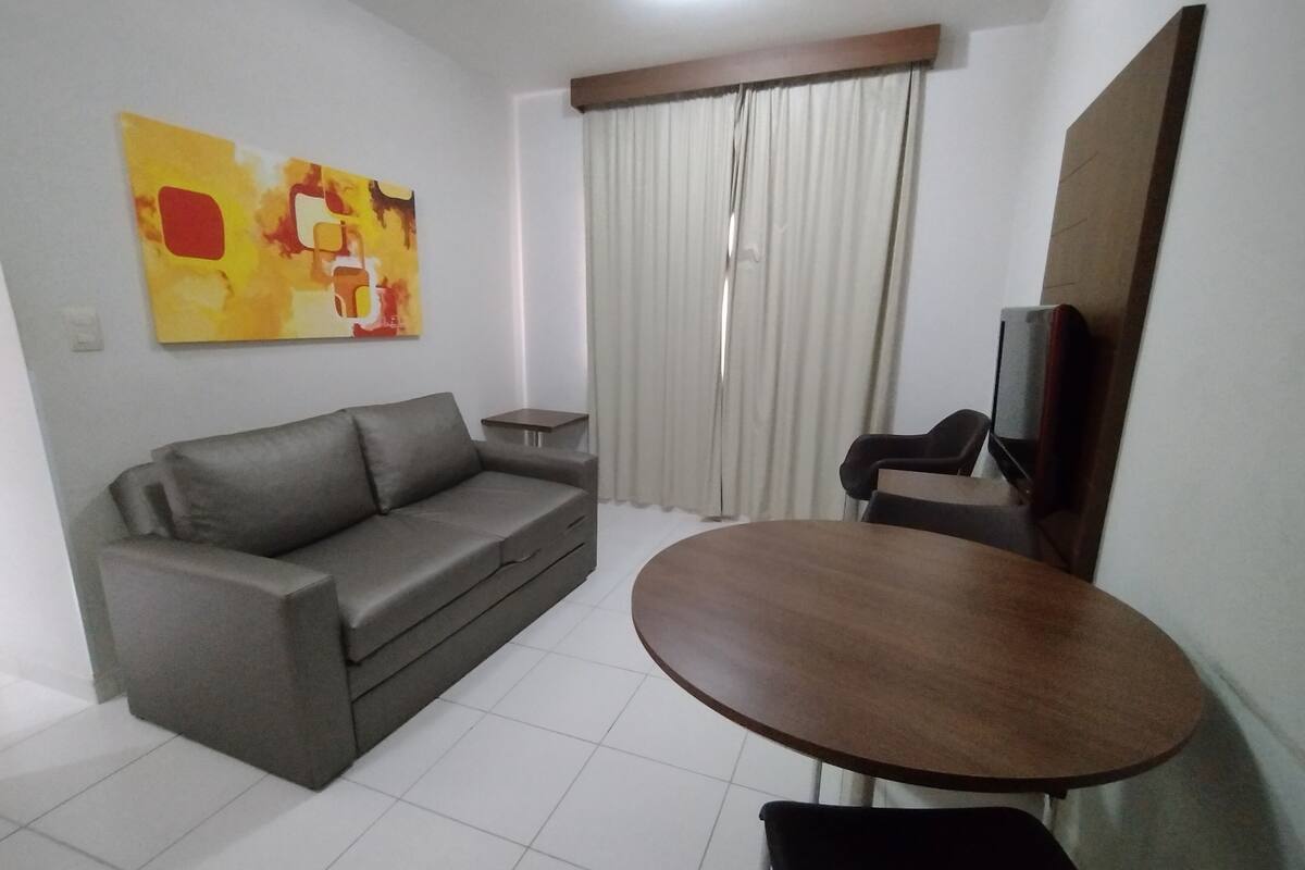 A living room with a grey sofa, a round wooden table, a TV, and a painting on the wall.