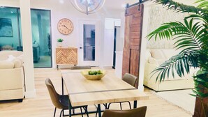 Een moderne woonkamer met een houten eettafel, twee bruine stoelen, een bank en een grote potplant.
