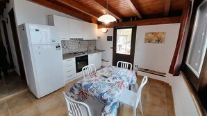 A compact kitchen with white cabinets, a stove, and a dining area with a table and chairs. - Villa Queen of the Sea - Top solarium and large garden (sciacca)