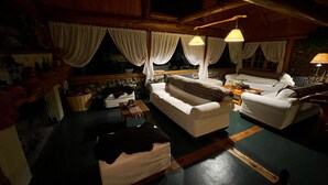 Ein gemütliches Wohnzimmer mit einer Couch, Sesseln und einem Couchtisch. Vorhänge, eine Lampe und ein Korb mit Gegenständen liegen auf dem Boden.