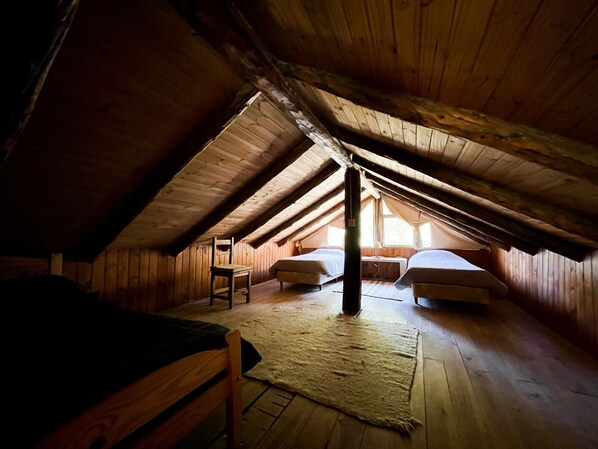 Une chambre confortable située dans les combles, avec des murs en bois et un plafond en pente. On y trouve deux lits, une chaise et une petite table.