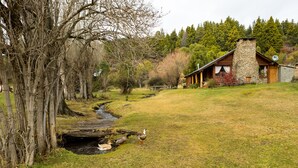 Eine rustikale Holzhütte mit einem Steinkamin, umgeben von einer grünen Landschaft und einem kleinen Bach.