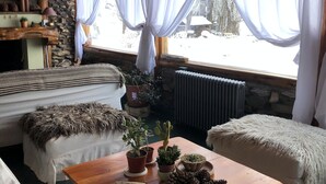 Ein gemütliches Blockhaus-Interieur mit Holztisch, zwei gepolsterten Bänken, einer Steinwand und einem Fenster mit Vorhängen.