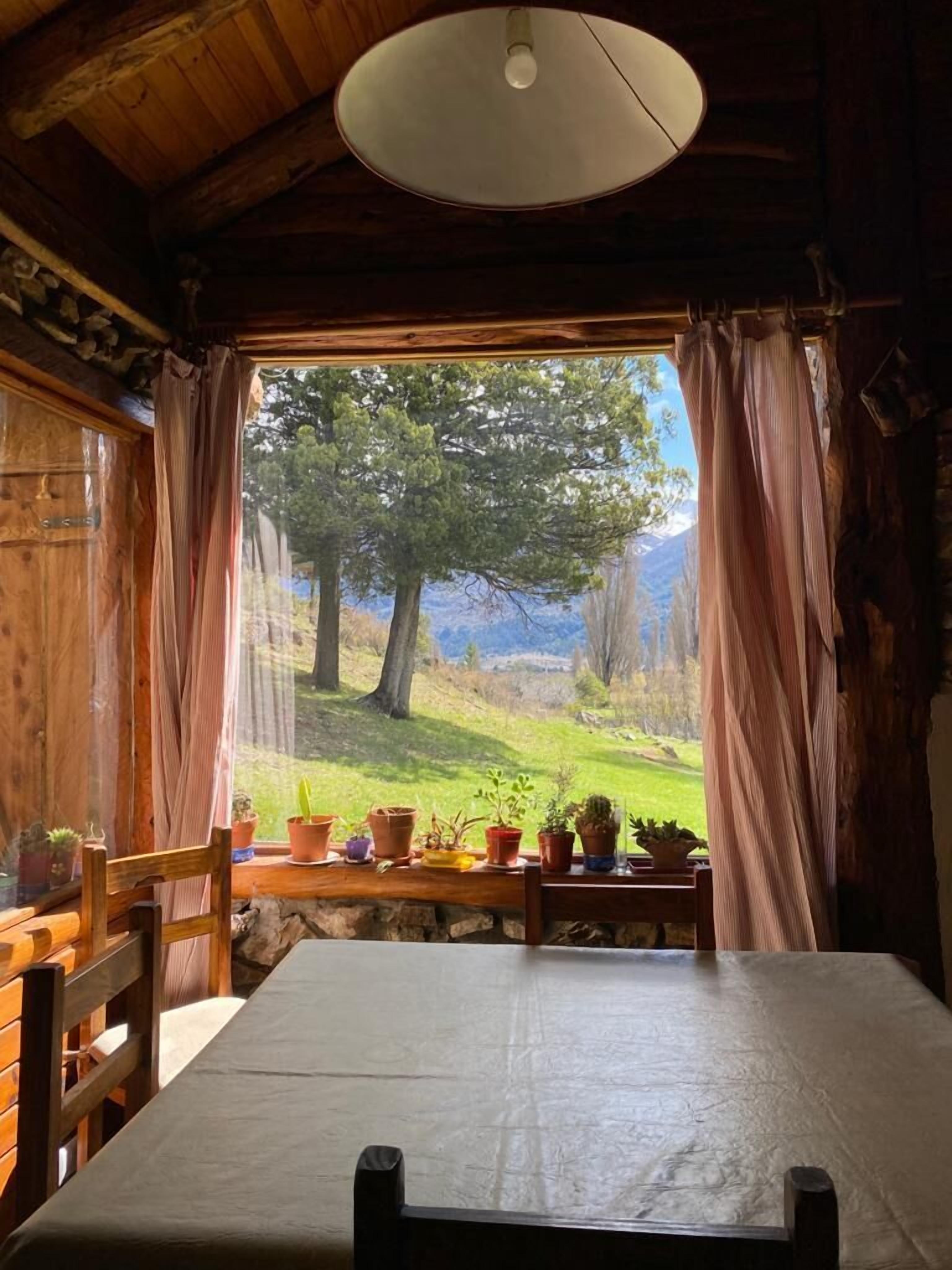 A rustic wooden cabin with a large window, a table, and chairs.
