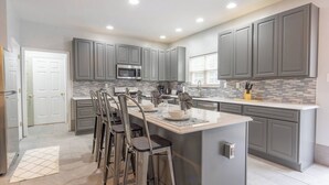 A modern kitchen with grey cabinets, a central island, bar stools, and a microwave.