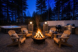 A patio with a fire pit, outdoor seating, a hot tub, and a grill.
