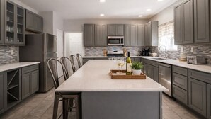 A modern kitchen with grey cabinets, a central island, stainless steel appliances, and a tiled backsplash.