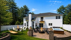 A two-story house with a patio area featuring a fire pit, outdoor seating, and a hot tub.