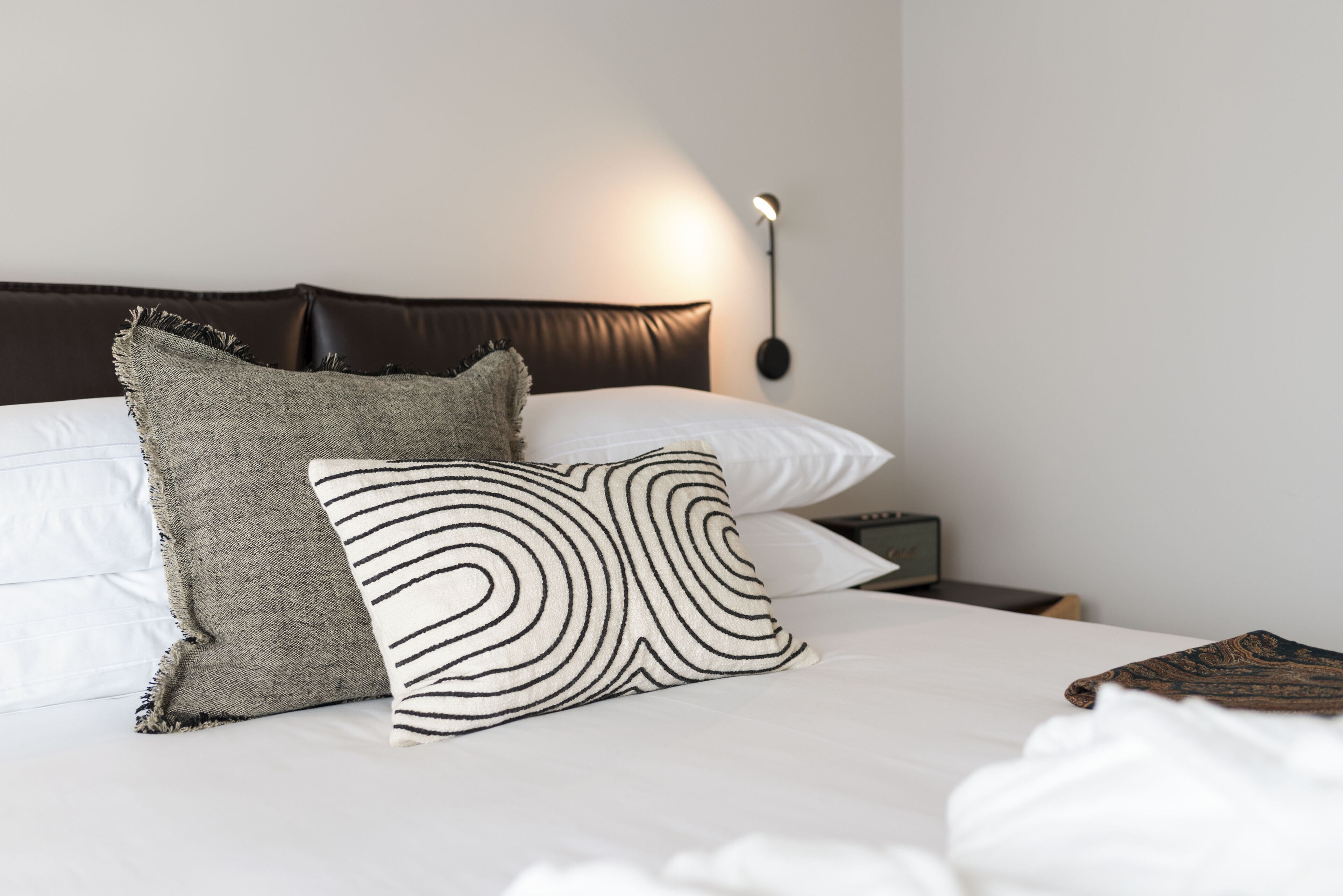 A neatly made bed with two pillows, a wall-mounted lamp, and a small bedside table.