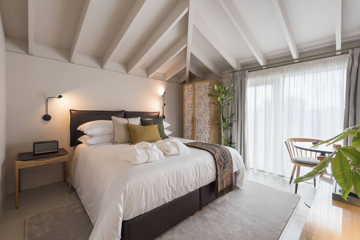 A modern bedroom with a large bed, bedside tables, a desk, and a chair.