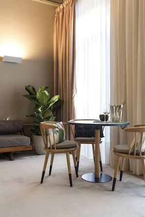 Ett modernt vardagsrum med ett runt glasbord, två trästolar, en stor grön växt och en soffa.