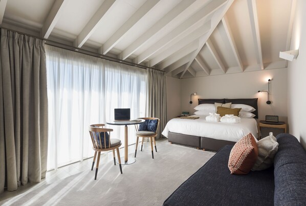 A modern hotel room with a large bed, a desk with a laptop, two chairs, and a sofa.