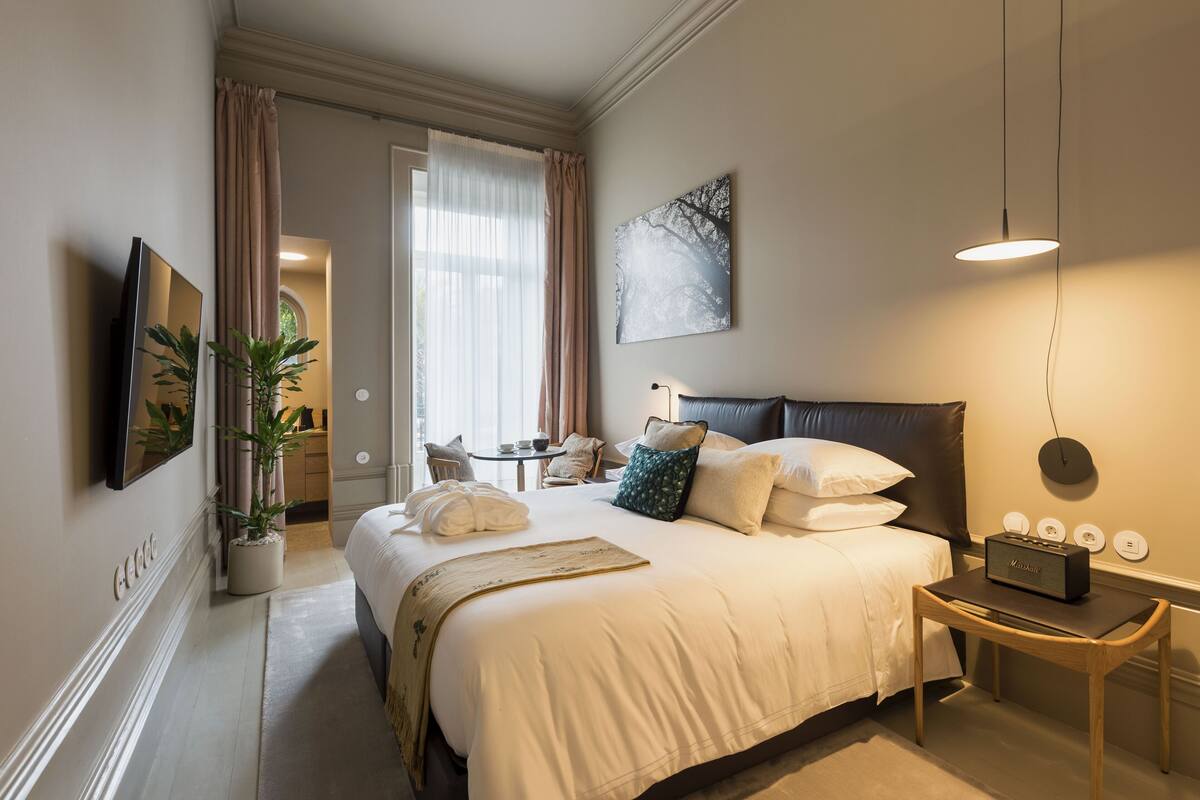 A hotel room with a large bed, a bedside table with a radio, a potted plant, and a view of the hallway.