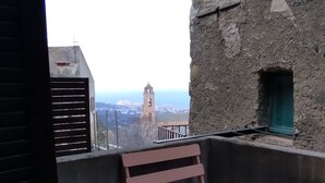 A balcony with a view of a distant tower, a stone wall, and a small window. - 2-bedroom apartment 5 km from the beautiful beaches of Ile Rousse (Santa-Reparata-Di-Balagna)