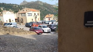A parking area with various cars, a stone-paved ground, and buildings with red-tiled roofs in the background. - 2-bedroom apartment 5 km from the beautiful beaches of Ile Rousse (Santa-Reparata-Di-Balagna)
