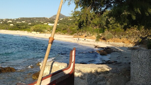A boat with a wooden pole, a stone wall, and a beach with people in the background. - 2-bedroom apartment 5 km from the beautiful beaches of Ile Rousse (Santa-Reparata-Di-Balagna)