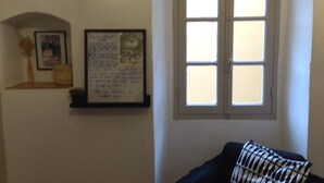 A room with a dark blue sofa, a window with white shutters, a framed quote on the wall, and a small plant on a shelf. - 2-bedroom apartment 5 km from the beautiful beaches of Ile Rousse (Santa-Reparata-Di-Balagna)