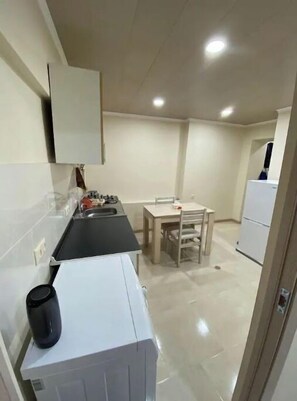 A compact kitchen with a refrigerator, a sink, and a dining table with chairs.