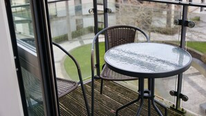 A balcony with a glass door, a round table, and two wicker chairs.
