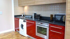 A compact kitchen with a washing machine, oven, microwave, and a coffee maker on the countertop.