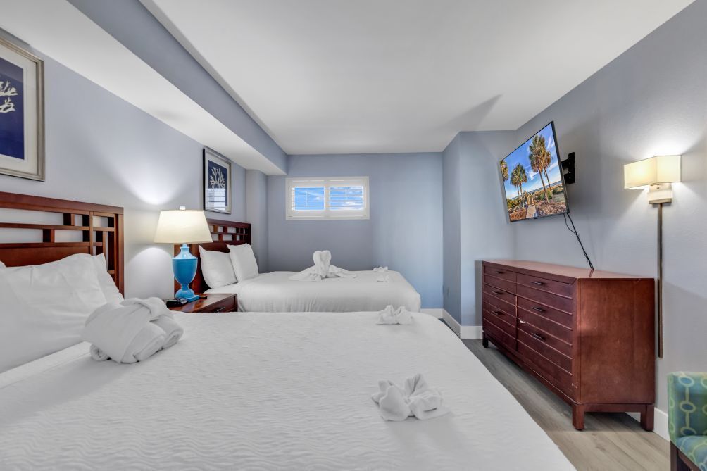 Een hotelkamer met twee bedden, een houten dressoir, een televisie en een raam met jaloezieën.