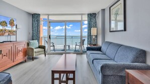 Un salon moderne comprenant un canapé, une table basse, un téléviseur et un balcon avec vue sur l’océan.