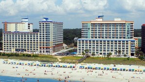 Un hôtel situé en bord de mer, composé de plusieurs immeubles de grande hauteur, avec une plage de sable et des parasols.