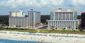 A beachfront hotel with multiple high-rise buildings, a sandy beach, and umbrellas.