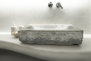 Eine freistehende Badewanne aus Stein mit Wasserhahn und Seifenspender auf einer weißen Arbeitsplatte.