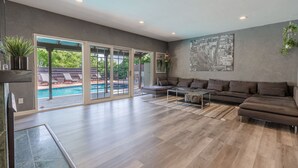 En rummelig stue med en stor modulsofa, et sofabord og udsigt til en swimmingpool gennem glasdøre.