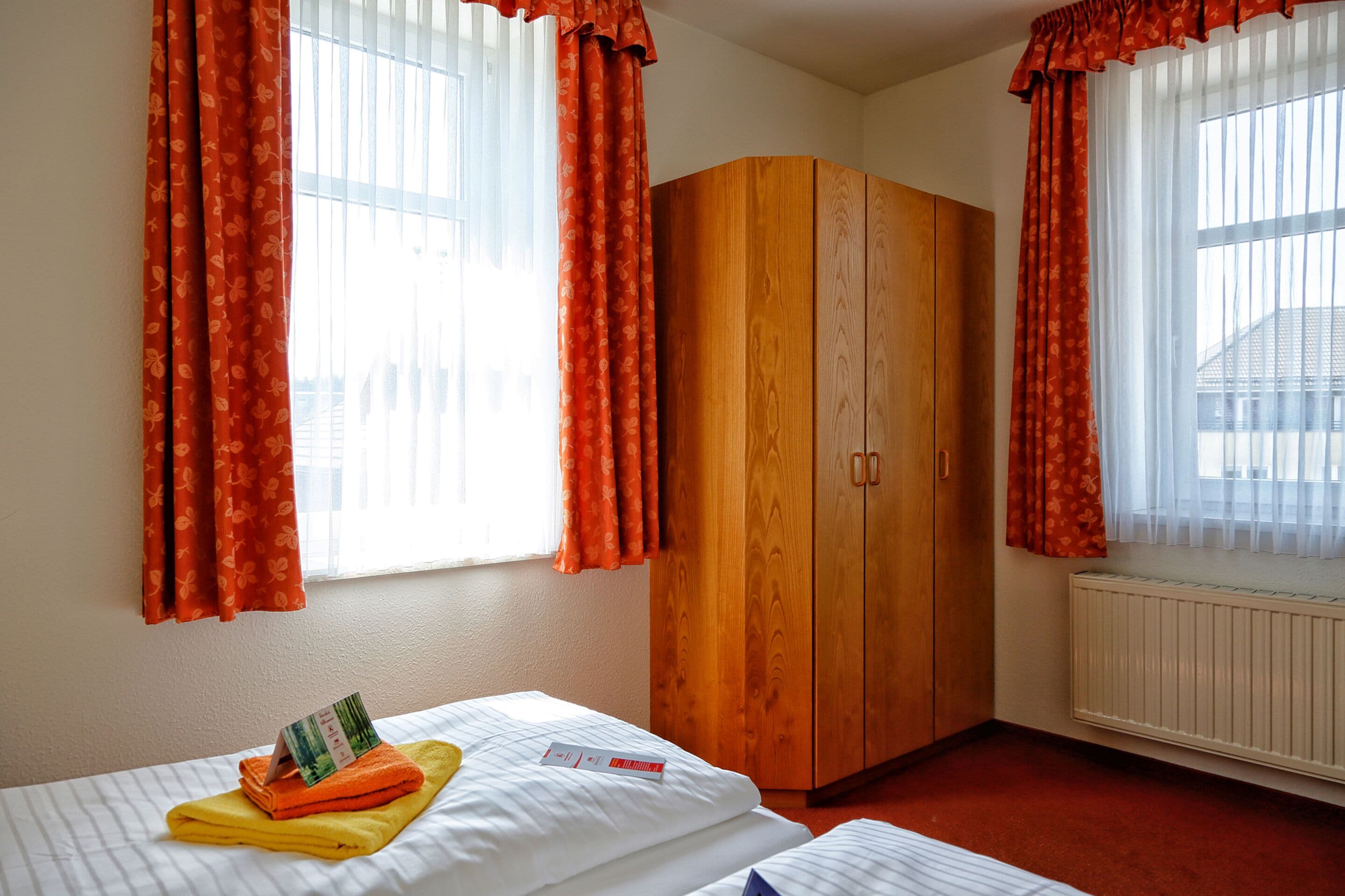 Ein Hotelzimmer mit zwei Betten, einem Holzschrank und Vorhängen.