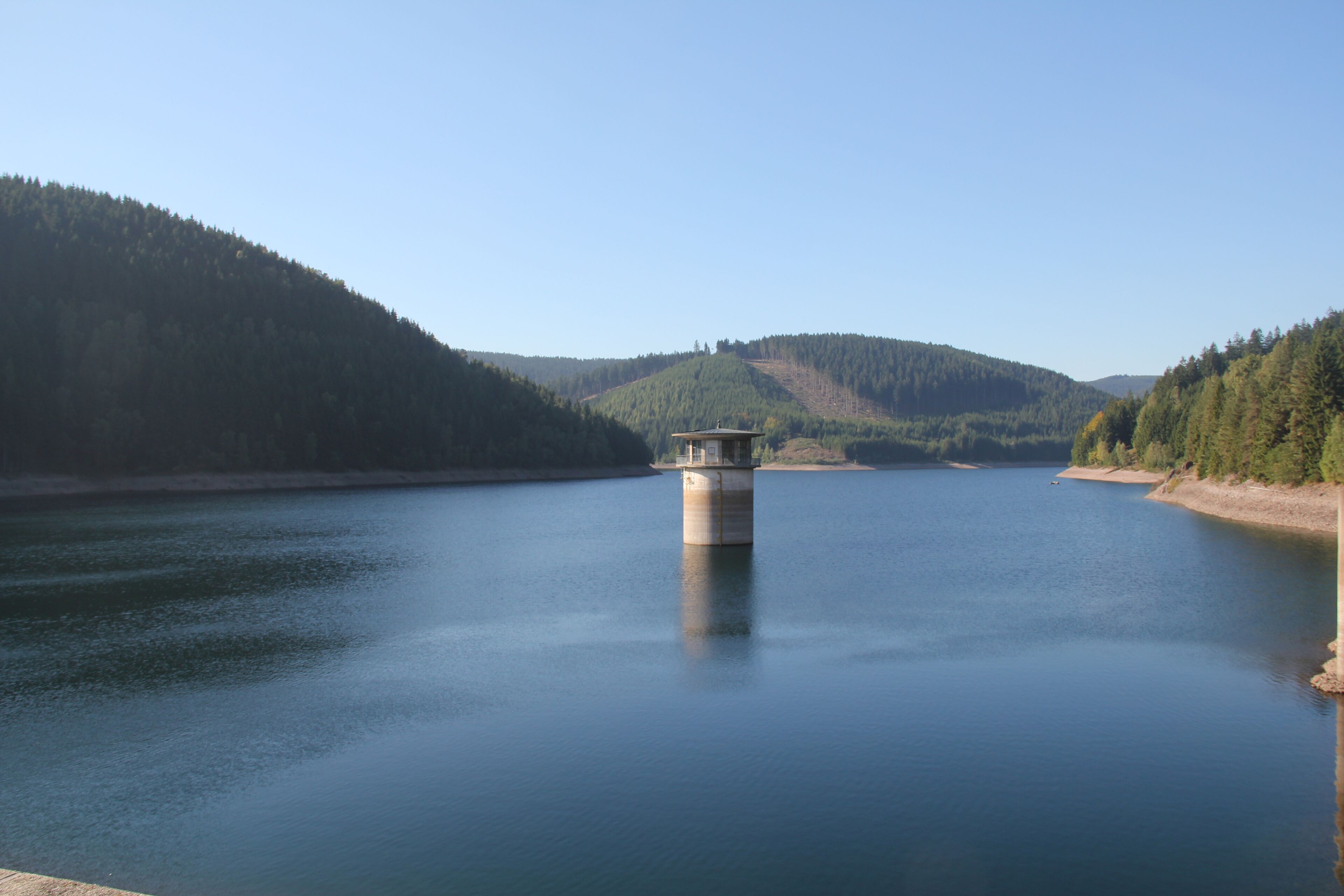 A calm lake with a small island in the center and forested hills in the background.