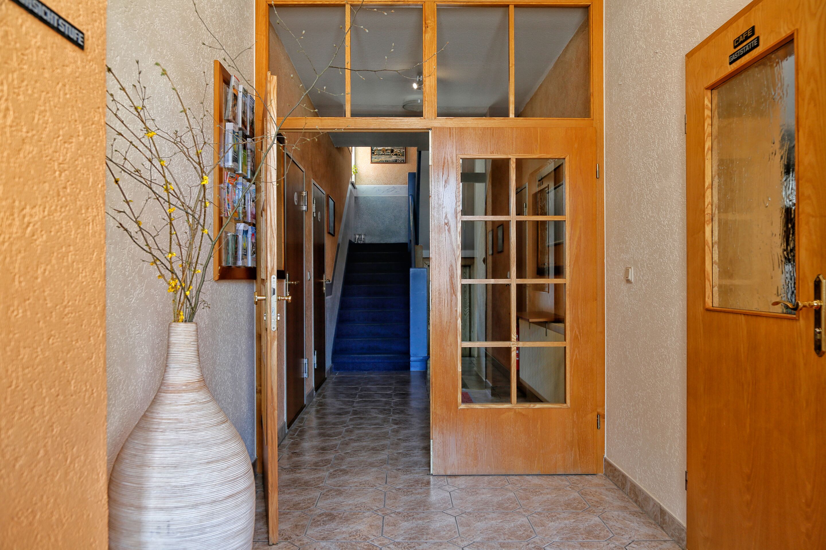 A hallway with a large wooden door, a staircase, and a vase with flowers.