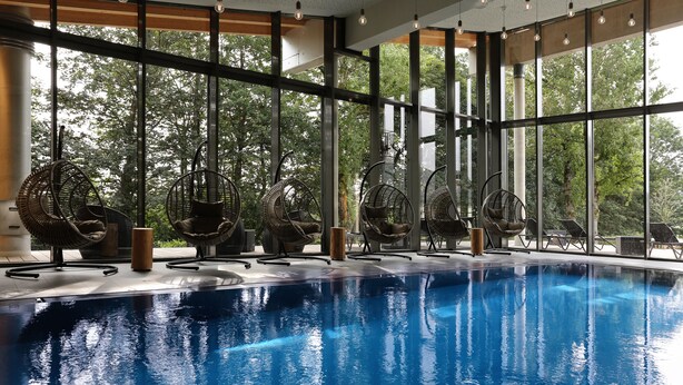 Una piscina interior con sillas de mimbre y ventanas amplias.