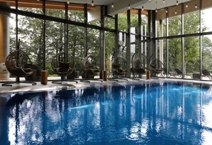 Una piscina interior con sillas de mimbre y ventanas amplias.