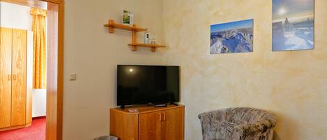 Una habitación con un armario de madera, un televisor, un sillón estampado y dos cuadros en la pared.