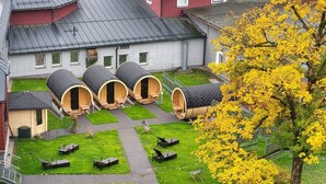 Un patio con cuatro cabañas de sauna de madera, una zona verde con asientos exteriores y un árbol de hojas amarillas.