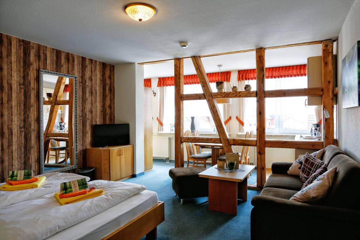 A hotel room with a bed, a sofa, a desk, a TV, and a window with curtains.