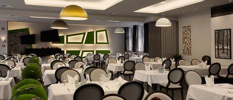 A dining area with multiple tables and chairs, a flat-screen TV mounted on the wall, and a modern ceiling design with recessed lighting.