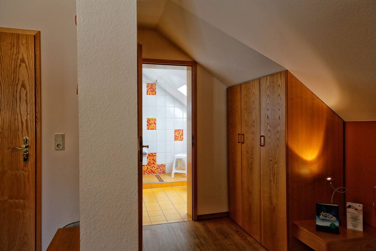 A hallway with wooden doors, a white wall, and a tiled floor leading to a bathroom with a shower and a white stool.