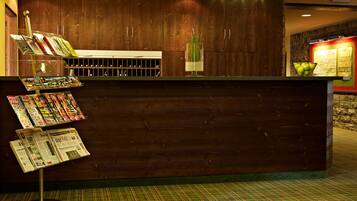 A reception desk with a wooden finish, a green patterned carpet, and a glass display case with magazines.