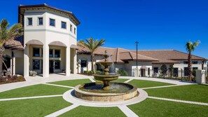 A courtyard with a central fountain, surrounded by well-maintained grass and palm trees.