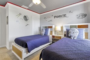 A bedroom with two beds, Star Wars-themed wall decals, and a ceiling fan.