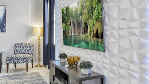 Un soggiorno moderno con una grande televisione, una poltrona a fantasia, una lampada da terra e piante decorative.