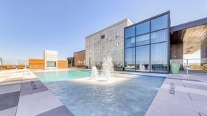 A rooftop pool with a water fountain, modern buildings, and a clear sky. - Laredo - Rooftop pool & Rainey St views (Austin)