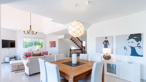 A spacious living area with a wooden dining table, white chairs, a chandelier, and a staircase leading to an upper floor. - Lovely vacation home with amazing views and private pool | Townhouse Calahonda (Mijas Costa)