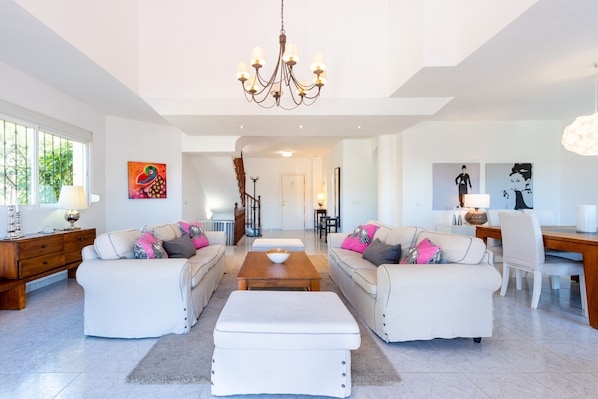 A spacious living room with two white sofas, a coffee table, and a chandelier.