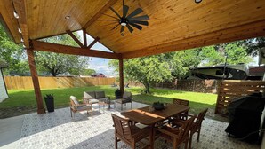 Eine überdachte Terrasse mit Holztisch und -stühlen, einem Deckenventilator und Blick auf den Garten.