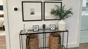 Eine Wand mit vier gerahmten Bildern, ein kleiner Tisch mit einem Blumentopf und zwei Korbwäschekörben.