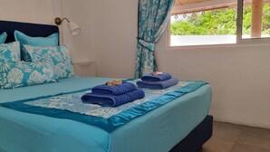 A bed with a floral-patterned headboard, a teal bedspread, and neatly folded towels on the side. - In the heart of the village villa 6 people not 8 (Moorea)